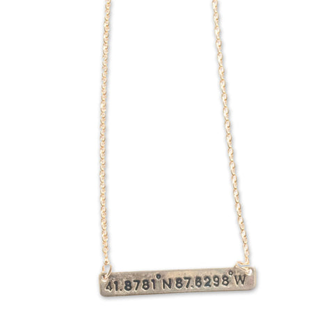 A gold-tone necklace with a bar pendant featuring the coordinates of Chicago.