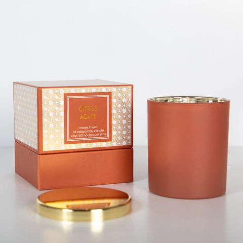 A boxed Citrus Agave candle with a gold foil design, the jar is sienna orange with a gold lid.