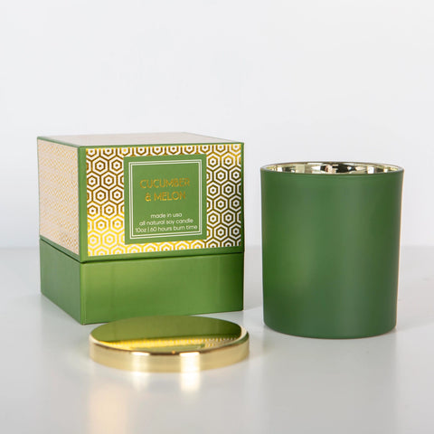 A green boxed candle with gold foil design on the lid, displayed alongside its packaging box. The candle is shown with the lid off.