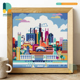 A diamond painting kit depicting a colorful cityscape, completed and framed, placed on a table next to a cup.