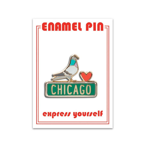 An enamel pin with a pigeon and a heart, sitting on a green Chicago street sign.