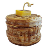 A candle designed to resemble a stack of waffles with butter and syrup on top, made from natural soy wax.